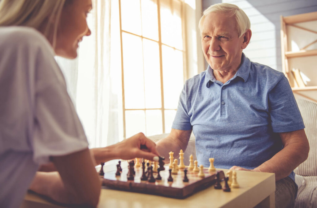An adult female is playing a chess board with her senior father.