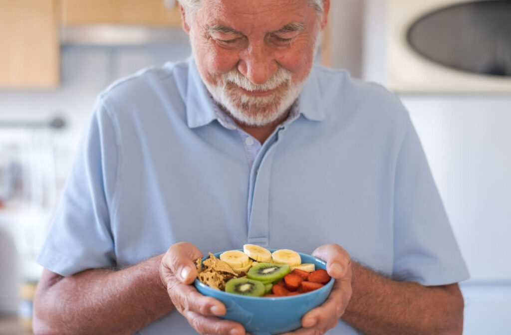 A senior man is holding a bowl of cereal and fruits for breakfast.
