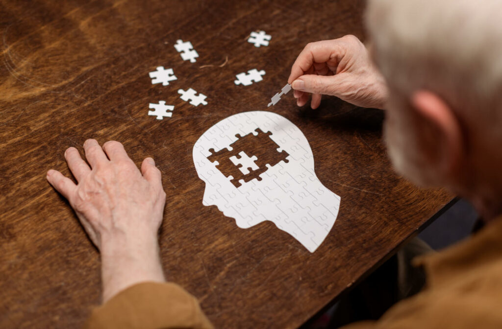 A senior man completing a jigsaw puzzle shaped like the profile of a person's head.
