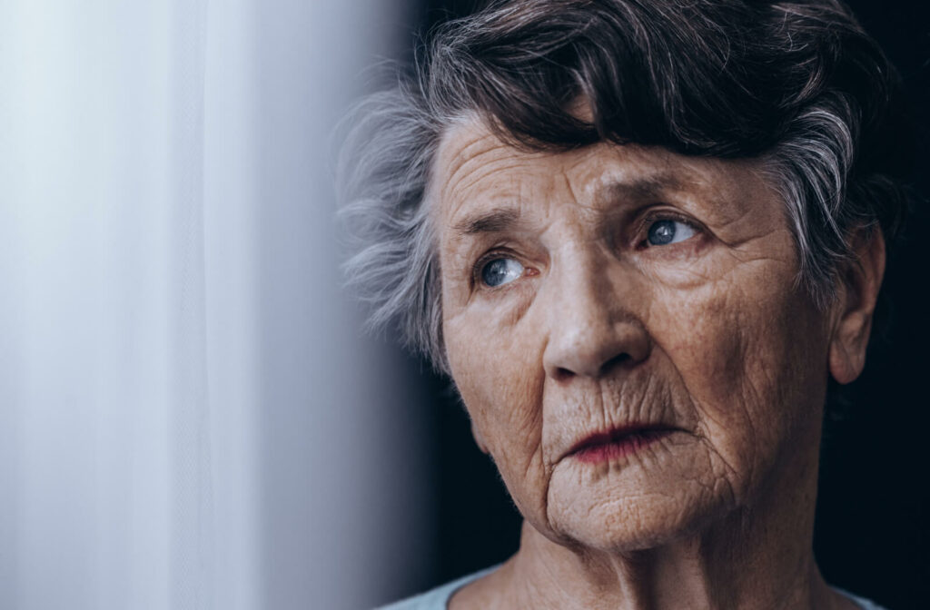 A portrait of an old woman standing beside a window and staring outside.