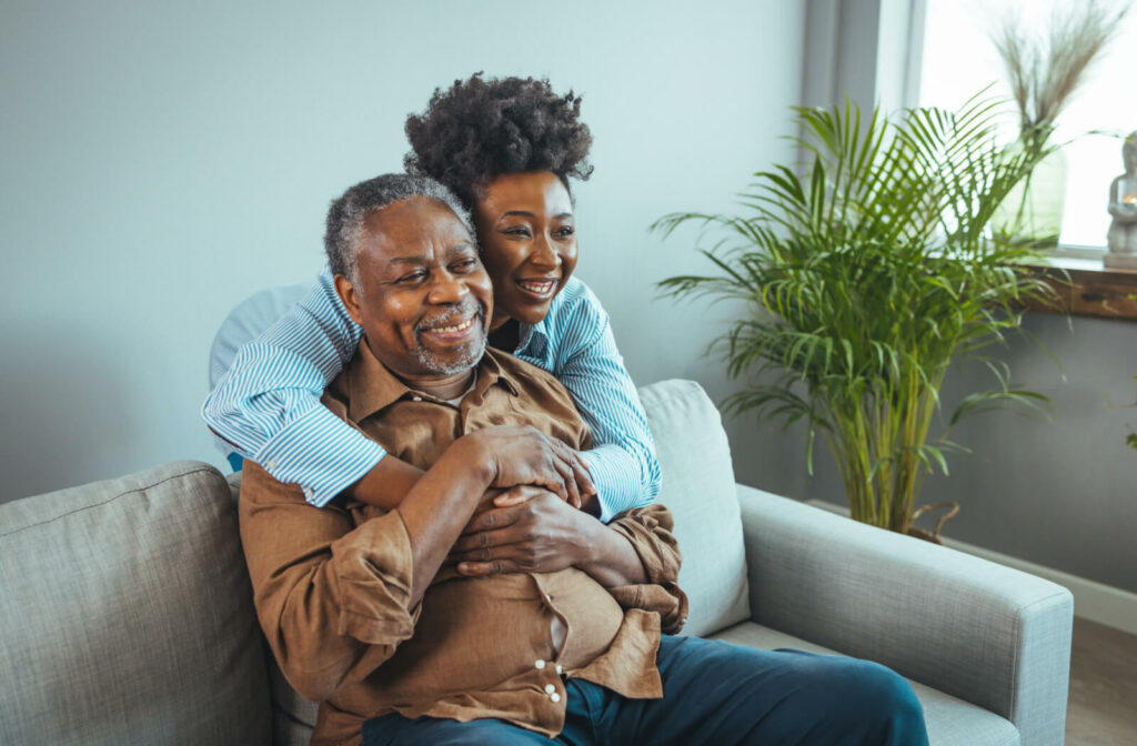 An older adult man with his daughter hugging him in a living room