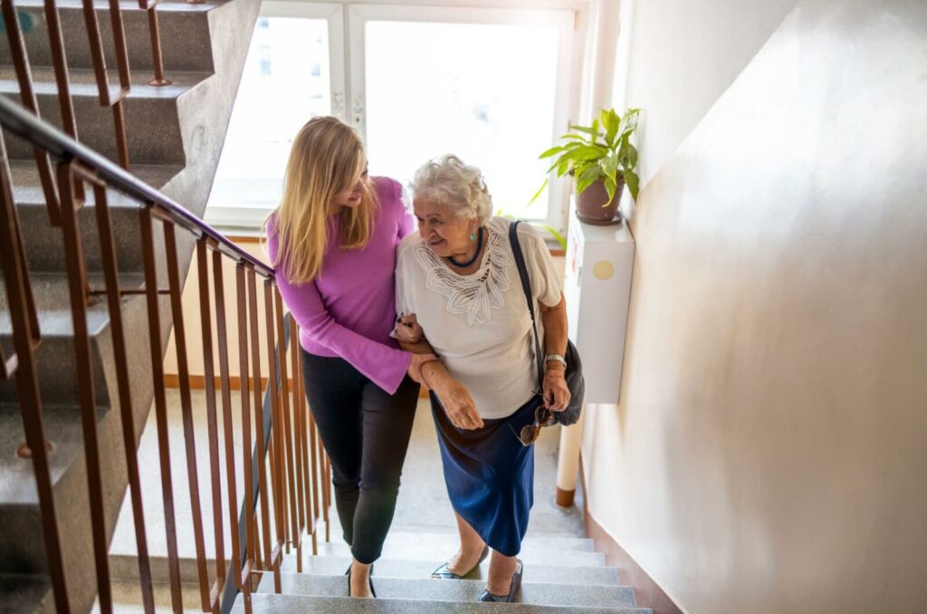 A smiling staff member in hospice care providing comfort to an older adult lying in bed by holding his hand and putting her arm around his shoulder.