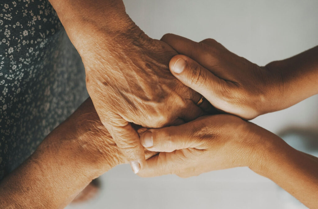 An adult comfortingly holds a senior’s hands, representing care and compassion for senior care