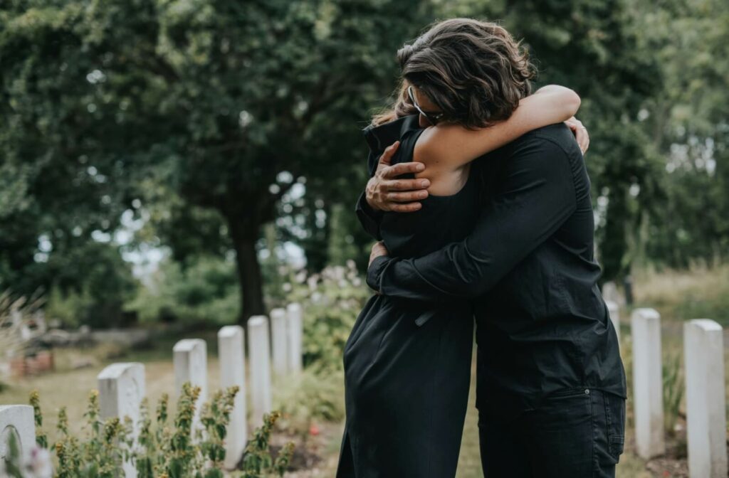 Two individuals hug each other tightly for emotional support after a funeral of a loved one